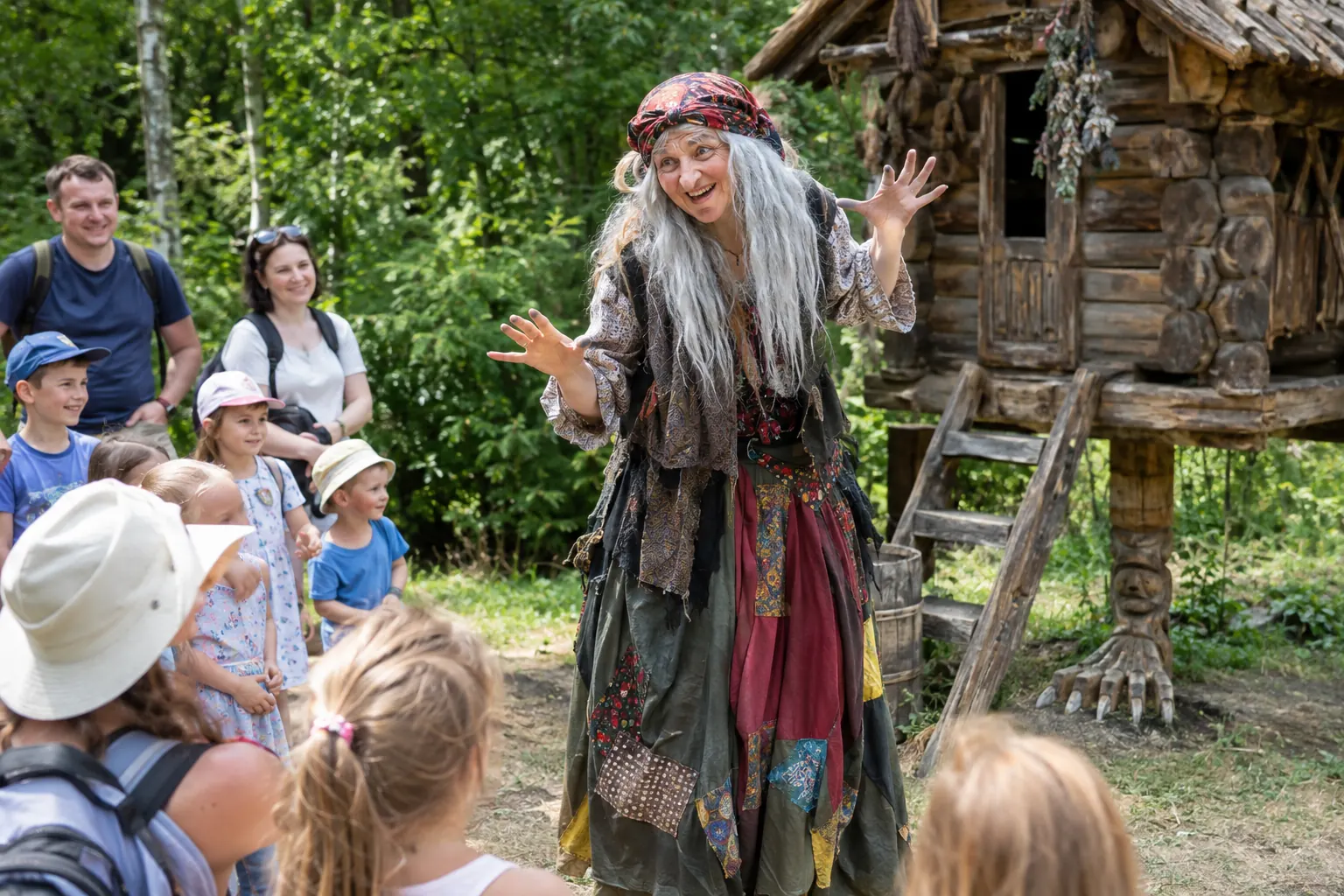 Người đóng vai Baba Yaga trong trang phục chắp vá vui vẻ kể chuyện cho các gia đình trước túp lều chân gỗ trong rừng