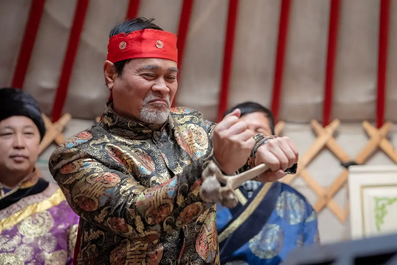 Người đàn ông mặc áo choàng thêu hoa văn kiểu Buryat, đội băng đô đỏ, trong lều yurt cùng mọi người